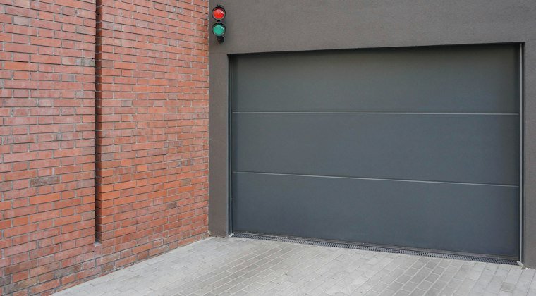 A grey garage door next to a brick wall